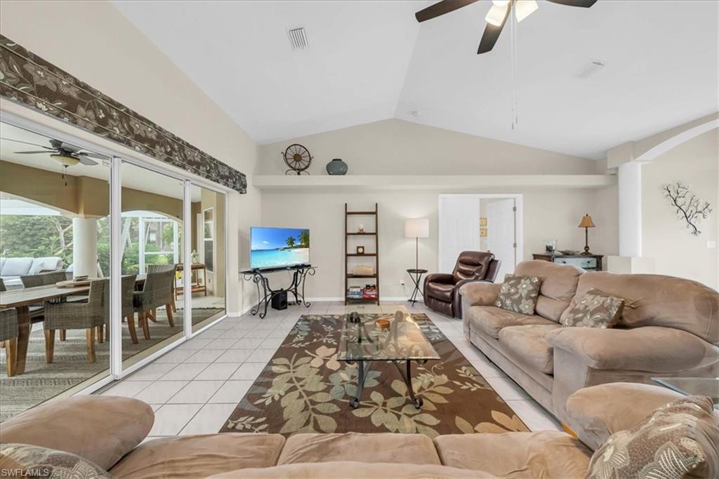 Living room featuring a ceiling fan, tile patterned flooring, a sunroom, arched walkways, and high vaulted ceiling