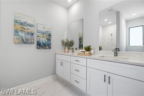 Bathroom with double vanity, light marble finish floors, and recessed lighting