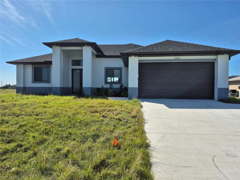 Prairie-style house with roof with shingles, concrete driveway, stucco siding, an attached garage, and a front yard