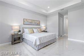 Bedroom featuring a raised ceiling, light marble finish flooring, and recessed lighting