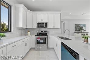 Kitchen with white cabinets, stainless steel appliances, a peninsula, decorative backsplash, and light stone countertops