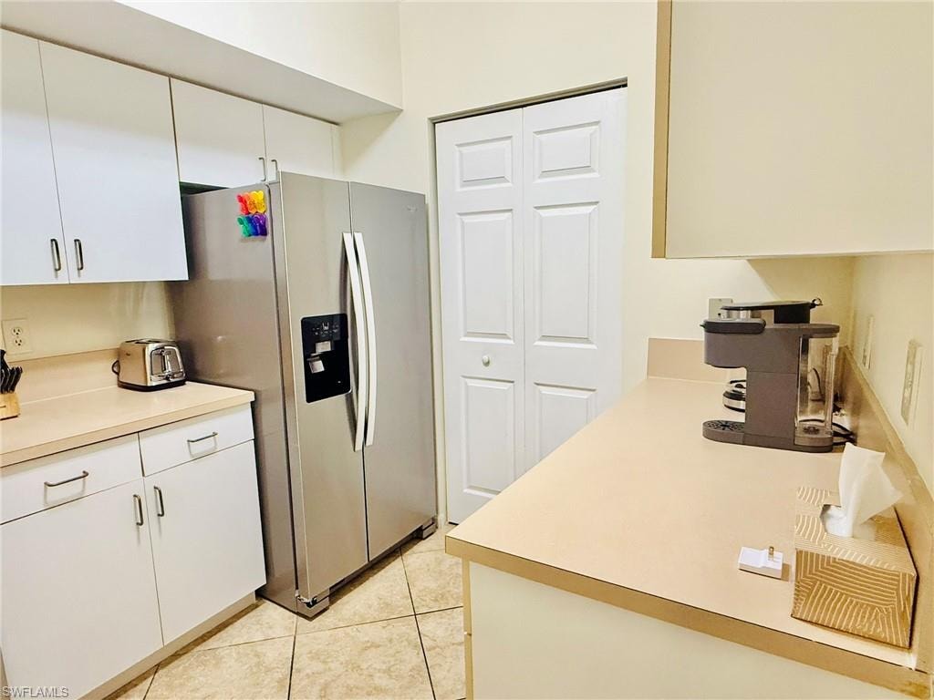 Kitchen with stainless steel fridge with ice dispenser, light countertops, white cabinets, and light tile patterned floors