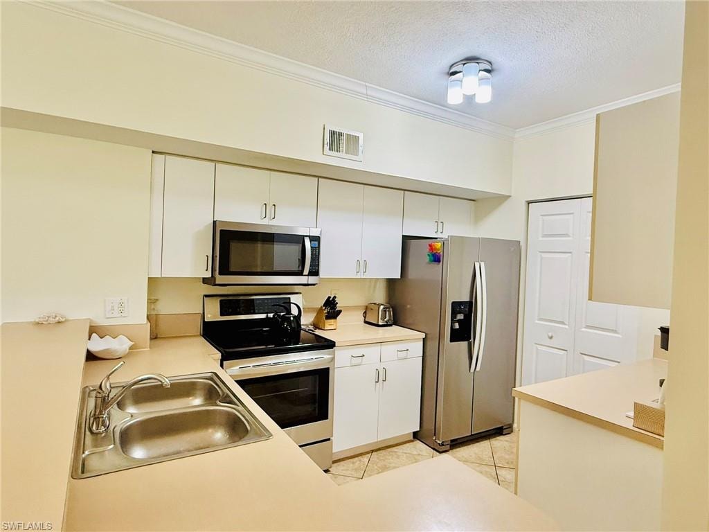 Kitchen with appliances with stainless steel finishes, ornamental molding, light countertops, a textured ceiling, and light tile patterned floors