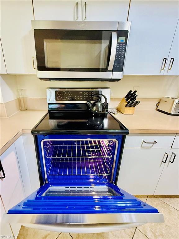 Kitchen view of stainless steel microwave, light countertops, white cabinetry, dishwashing machine, and range