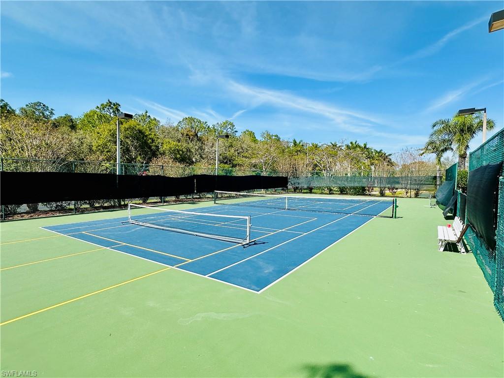 View of tennis court featuring community basketball court and view of wooded area