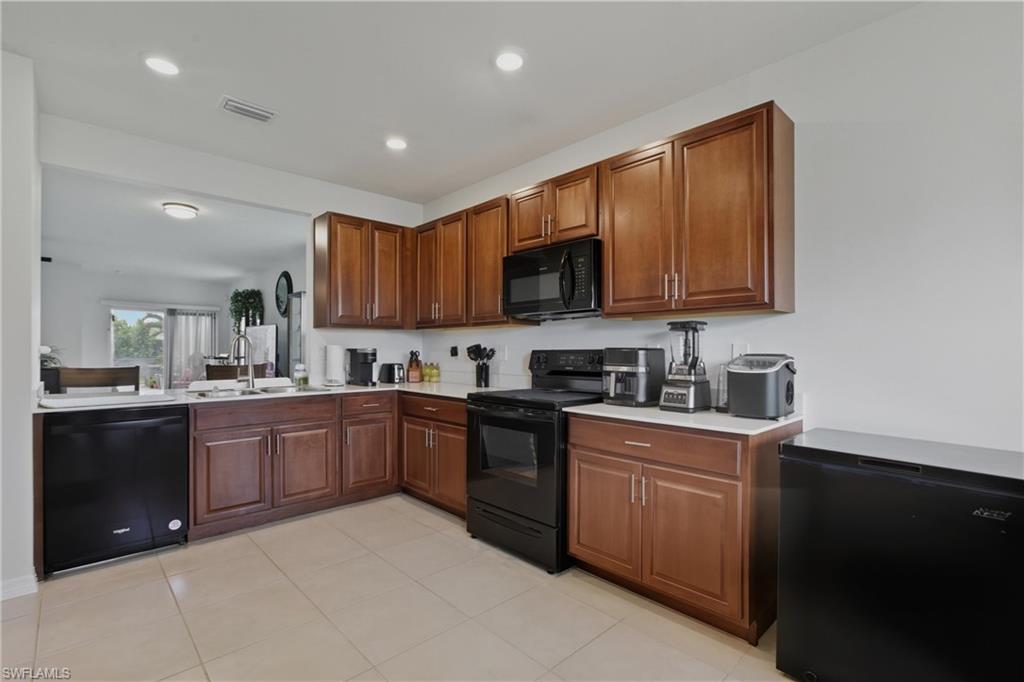 Kitchen with black appliances, light tile patterned floors, recessed lighting, and brown cabinetry
