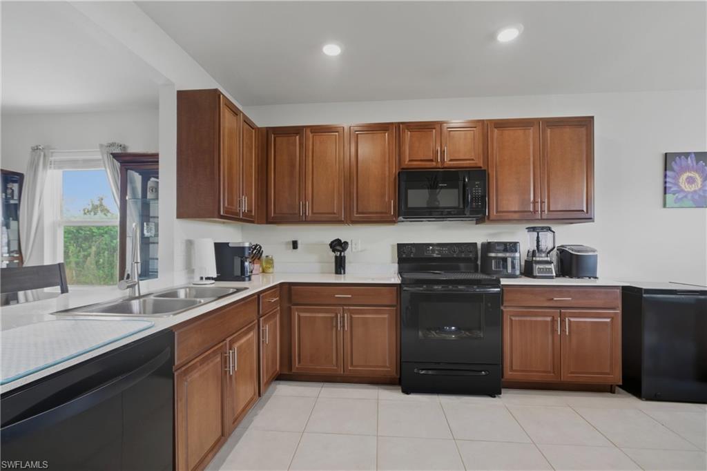 Kitchen featuring black appliances, light countertops, light tile patterned flooring, brown cabinetry, and recessed lighting