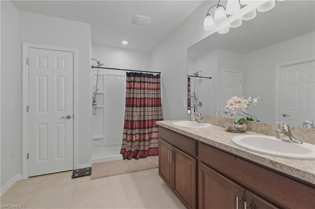 Bathroom featuring double vanity, light tile patterned flooring, and a shower stall