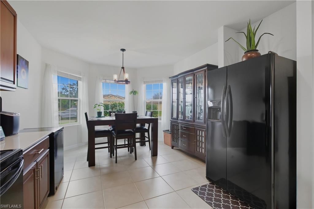 Kitchen with black appliances, decorative light fixtures, light tile patterned floors, a chandelier, and light stone countertops