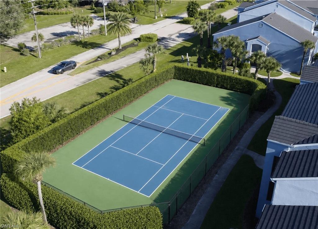 Full-size tennis court featuring a blue playing surface with white lines, surrounded by a green perimeter
