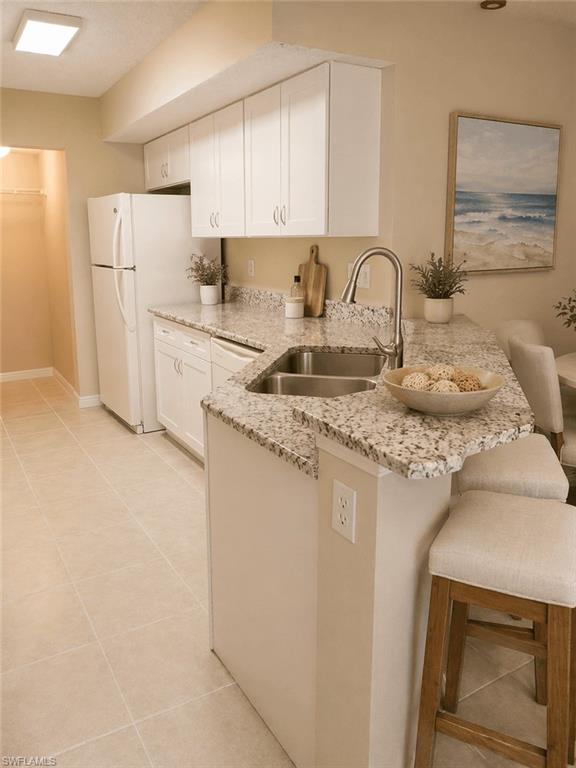 L-shaped kitchen island featuring a double basin stainless steel sink, gooseneck faucet, and light-toned stone-finish countertop