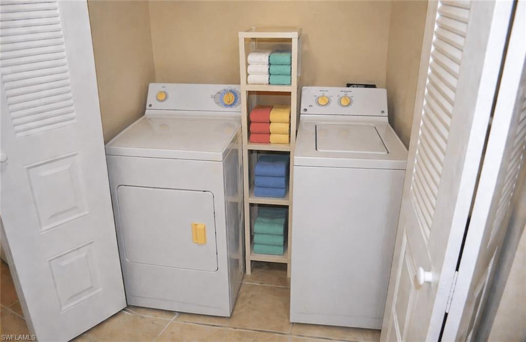 Dedicated laundry closet featuring a white washer and dryer set, neutral wall color, tiled flooring, and white louvered bifold doors