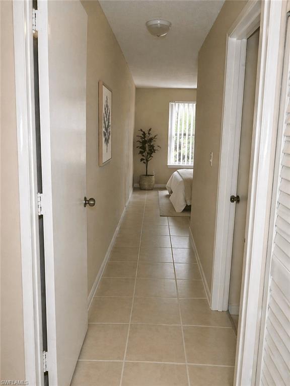 Hallway featuring neutral-toned tile flooring, light neutral wall paint, and a flush-mount ceiling light fixture