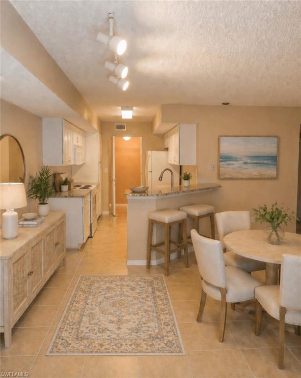 Open-concept kitchen and dining area featuring tile flooring, white cabinetry, a breakfast bar with seating, and track lighting