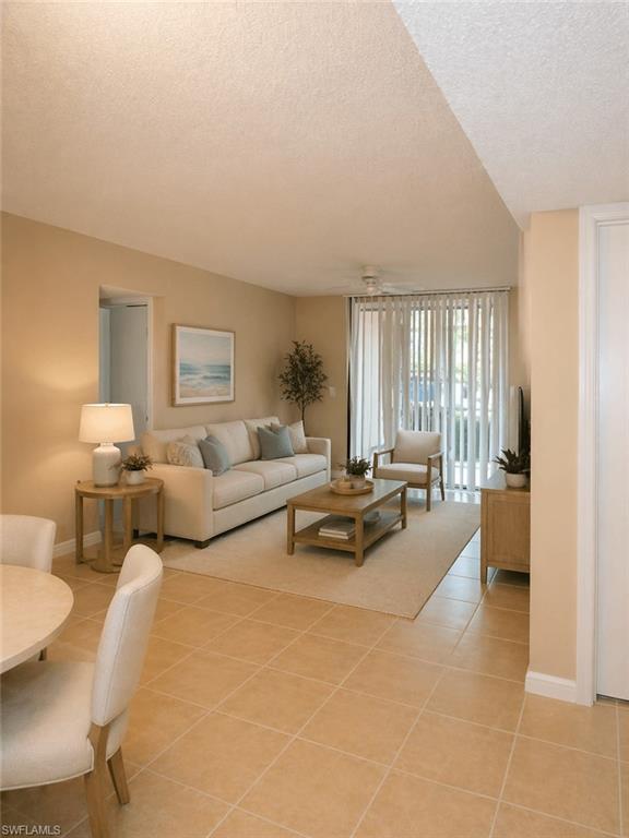 Open-concept living area featuring light-toned tile flooring, a sliding glass door with vertical blinds, and a neutral color palette