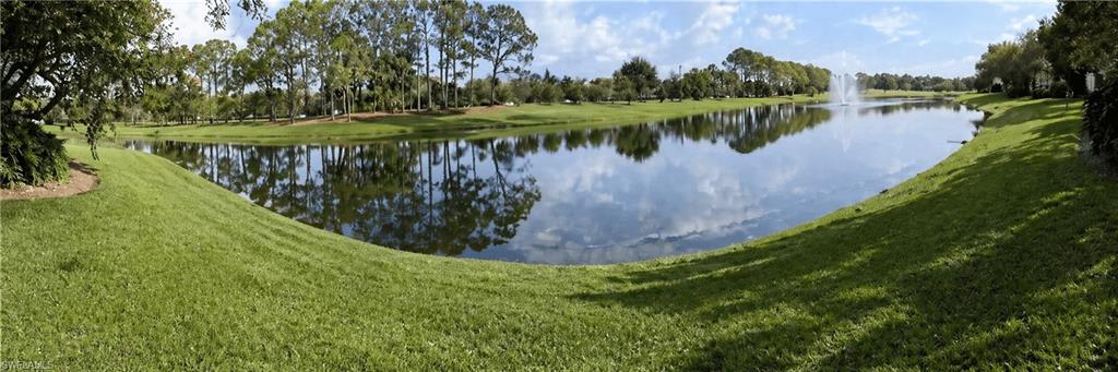 Expansive waterfront setting featuring a tranquil lake, lush green lawn, mature trees, and a decorative fountain