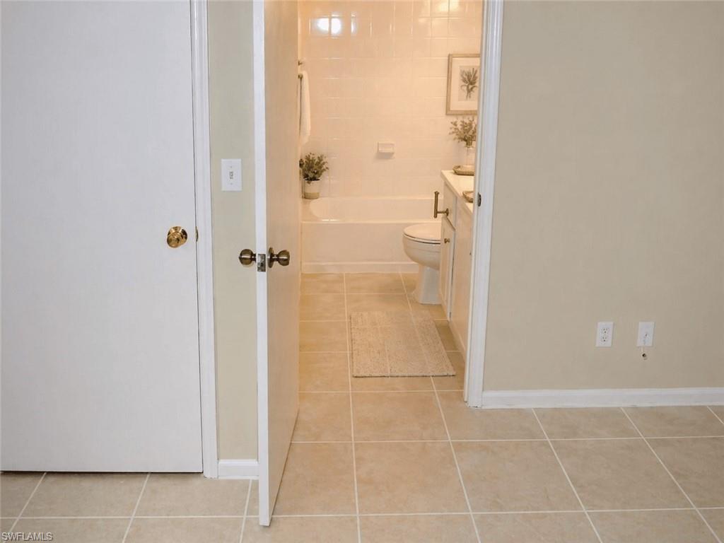 Bathroom featuring a tiled floor, white vanity with a countertop, toilet, and a bathtub with tiled surround