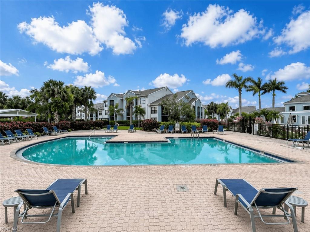 Expansive outdoor swimming pool with paver decking, surrounded by tropical landscaping, and multi-story residential buildings