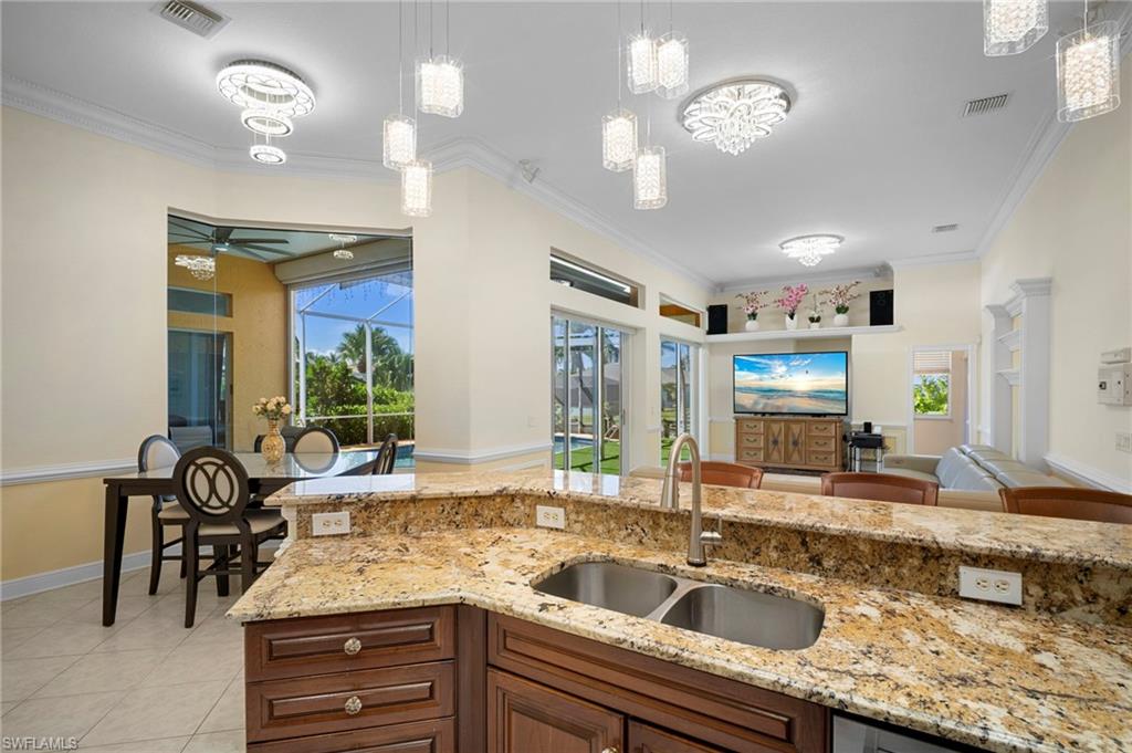 Kitchen featuring crown molding, light stone countertops, decorative light fixtures, light tile patterned flooring, and open floor plan