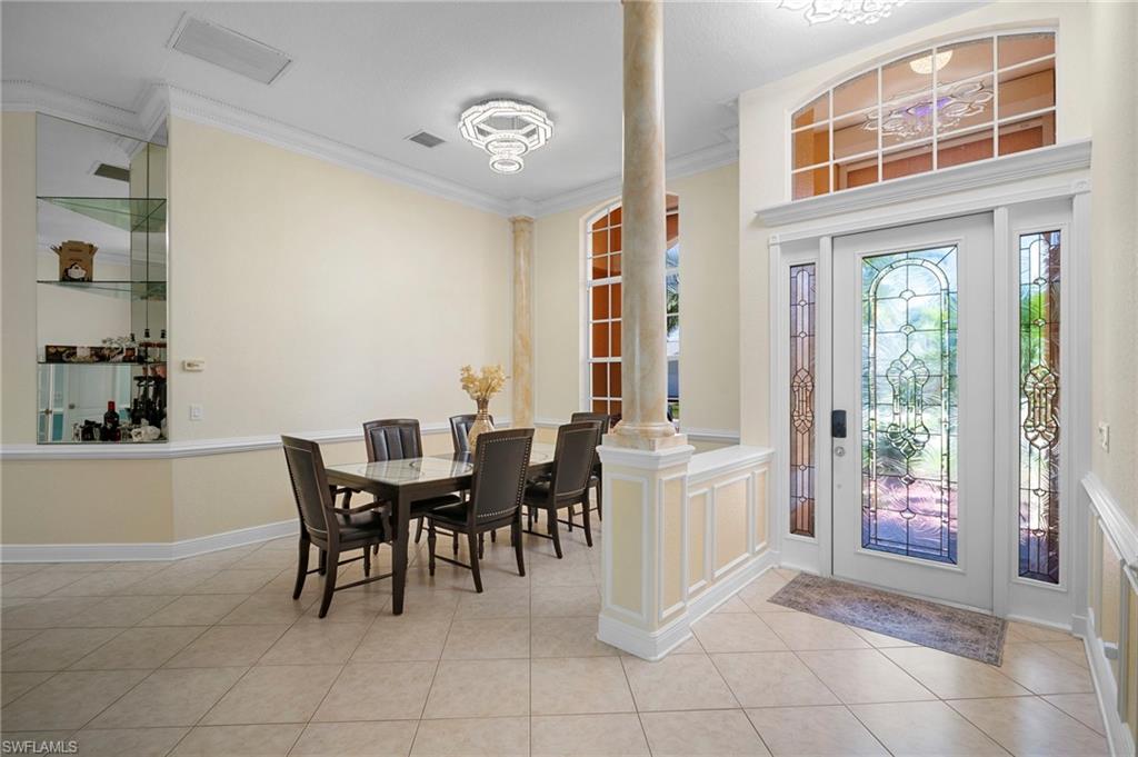 Entrance foyer with crown molding, light tile patterned flooring, ornate columns, and a chandelier