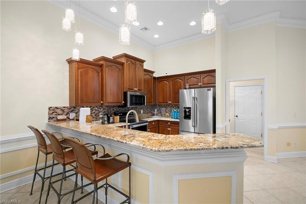 Kitchen with crown molding, light tile patterned flooring, appliances with stainless steel finishes, light stone counters, and a kitchen bar
