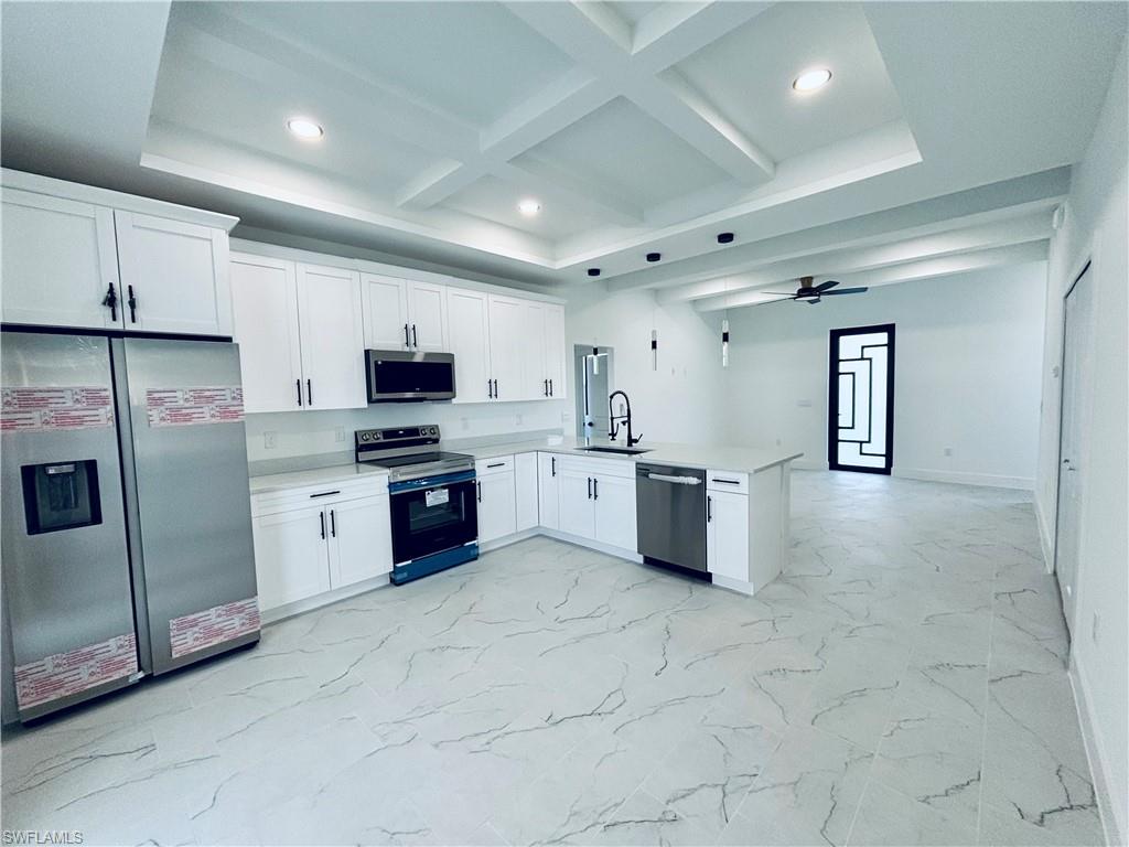 Kitchen with white cabinetry, stainless steel appliances, beam ceiling, light marble finish floors, and coffered ceiling