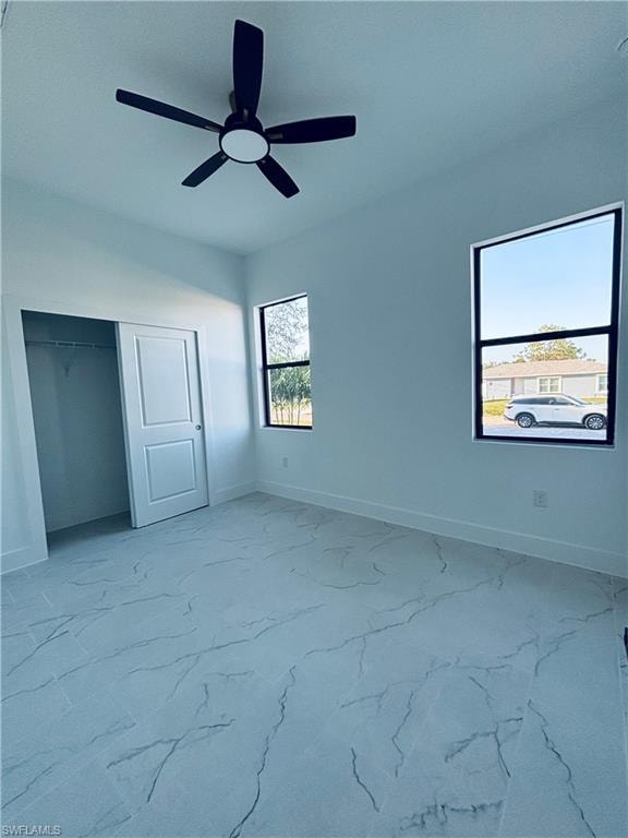 Unfurnished bedroom featuring light marble finish floors, ceiling fan, and a closet