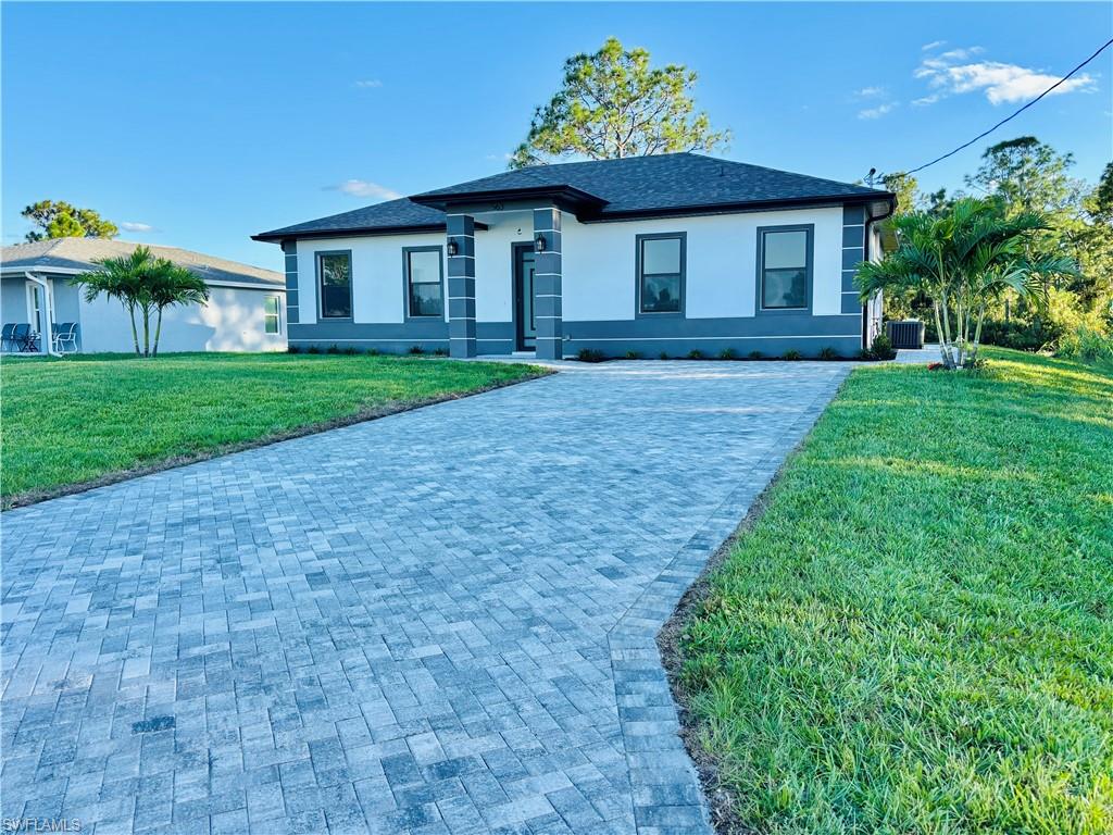 View of front of house featuring a front lawn, stucco siding, decorative driveway, and roof with shingles
