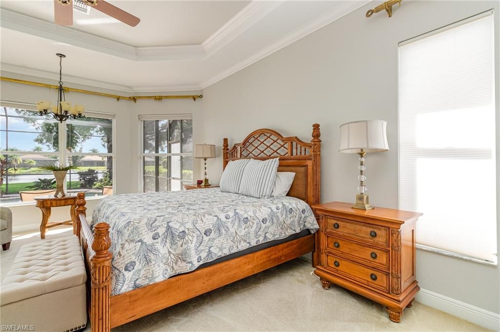 Carpeted bedroom featuring multiple windows, ceiling fan, a raised ceiling, crown molding, and a chandelier