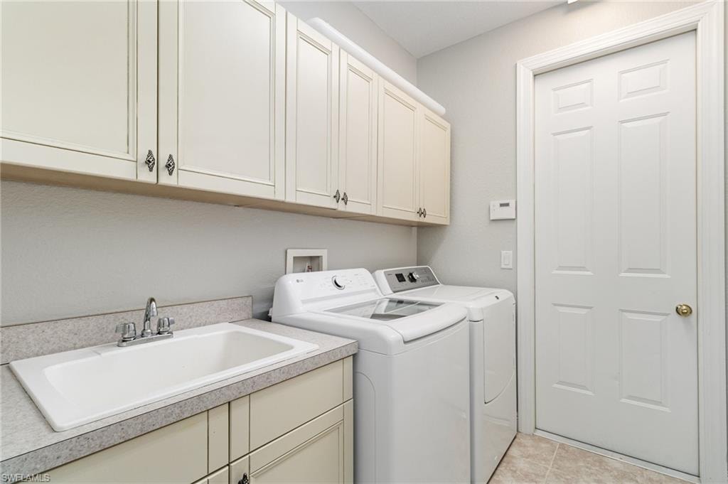 Laundry area with independent washer and dryer, light tile patterned flooring, and cabinet space