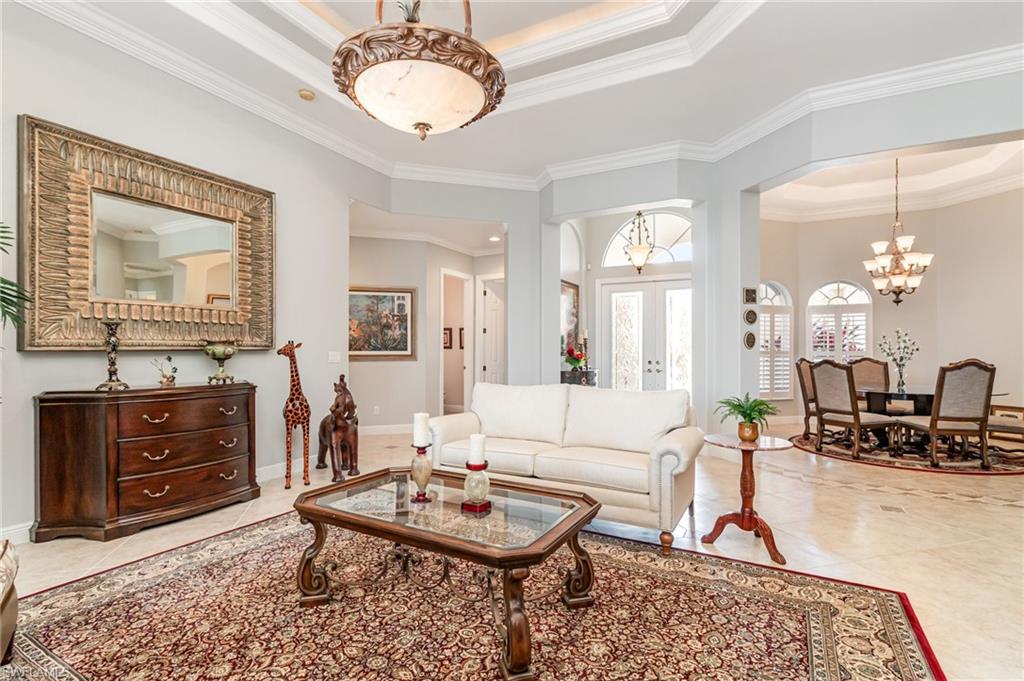 Living room featuring tile patterned floors, a chandelier, ornamental molding, a tray ceiling, and french doors