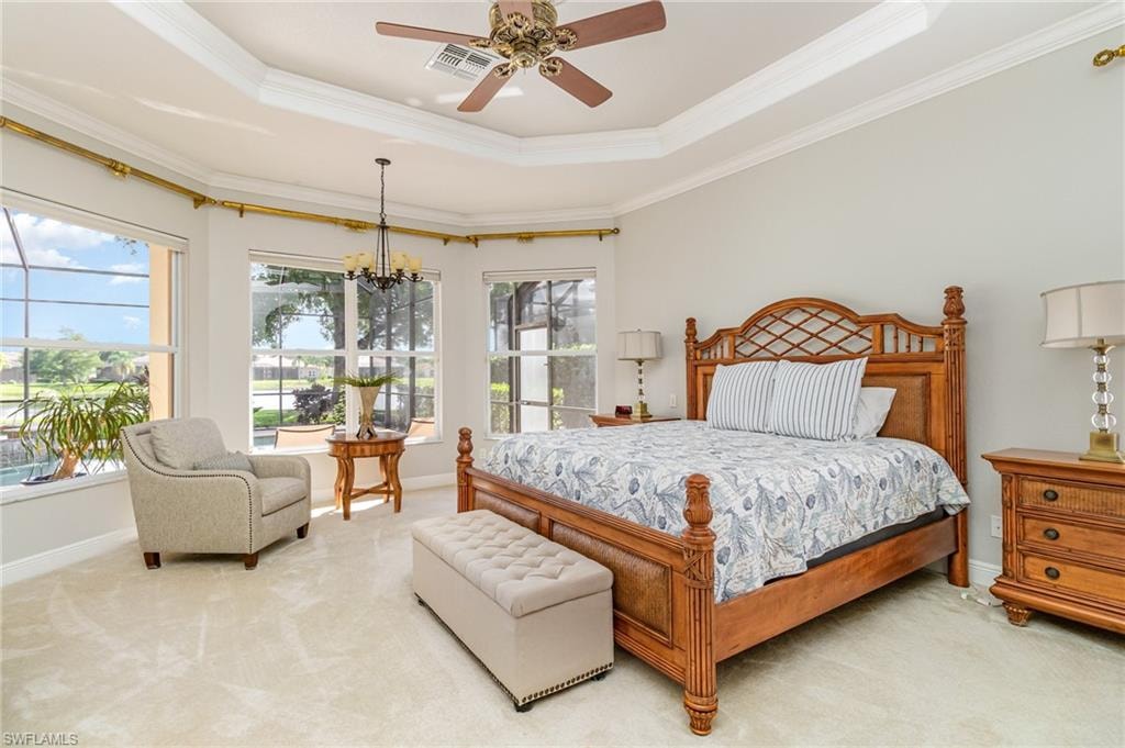 Bedroom with a tray ceiling, carpet floors, ornamental molding, ceiling fan, and a chandelier