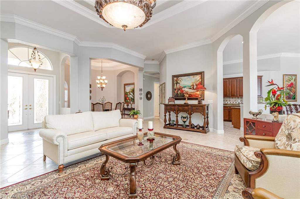 Living room featuring arched walkways, light tile patterned floors, french doors, a chandelier, and crown molding