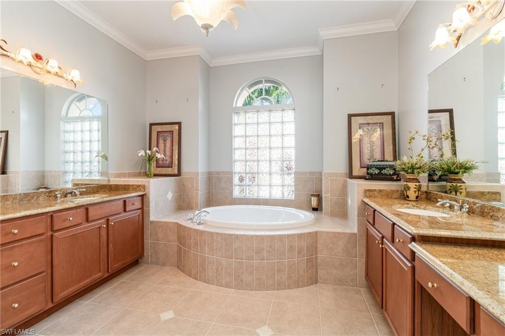 Full bathroom with two vanities, light tile patterned flooring, a bath, and ornamental molding