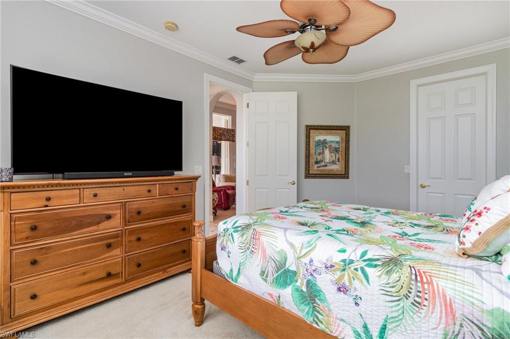 Bedroom featuring light carpet, crown molding, a ceiling fan, arched walkways, and ensuite bathroom