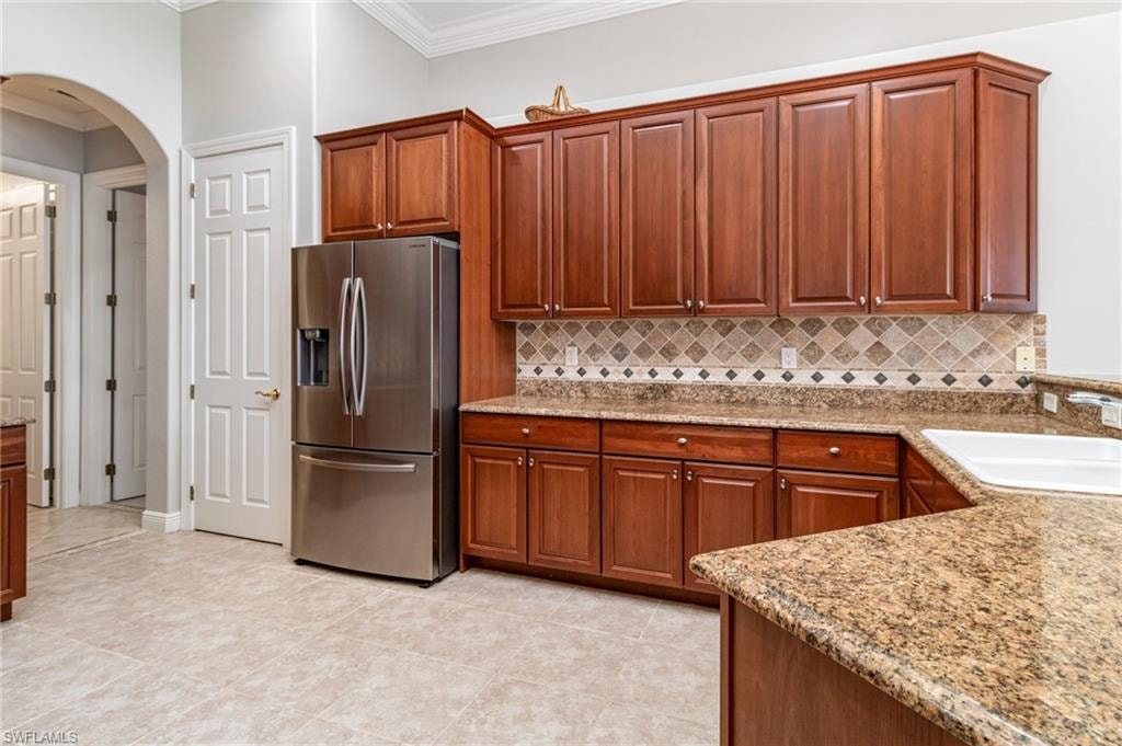 Kitchen featuring stainless steel refrigerator with ice dispenser, arched walkways, tasteful backsplash, ornamental molding, and brown cabinetry