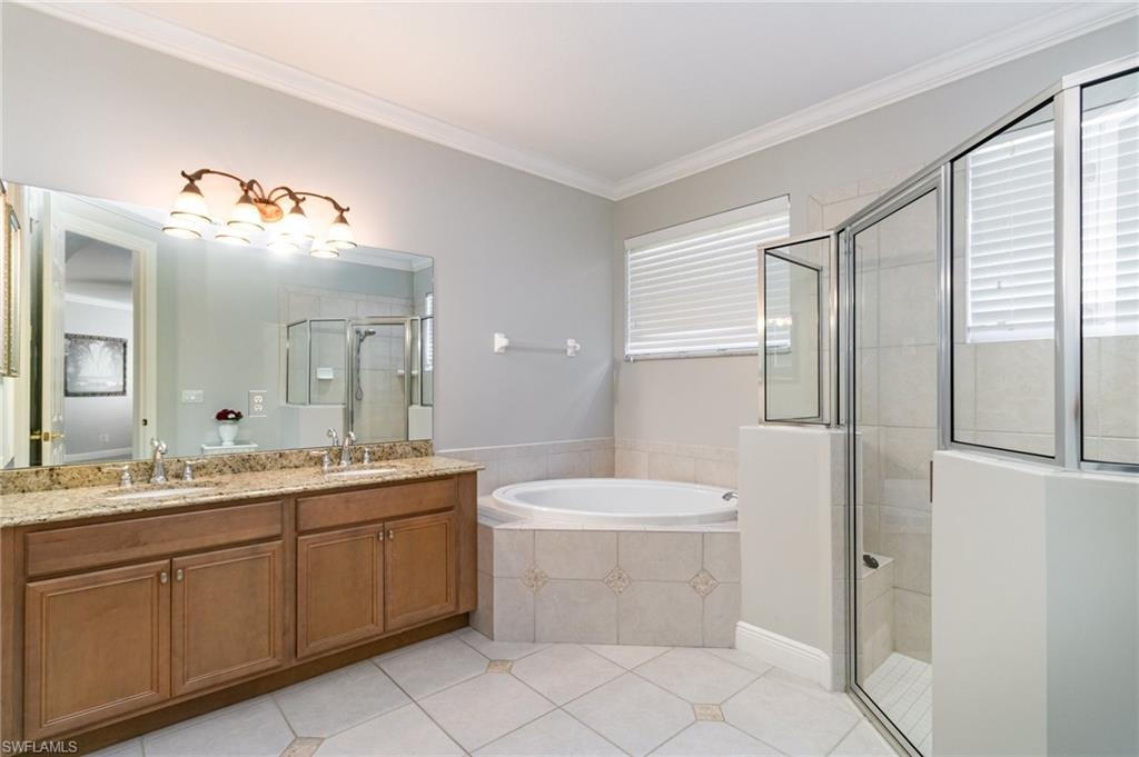 Bathroom with double vanity, a garden tub, ornamental molding, a shower stall, and light tile patterned floors