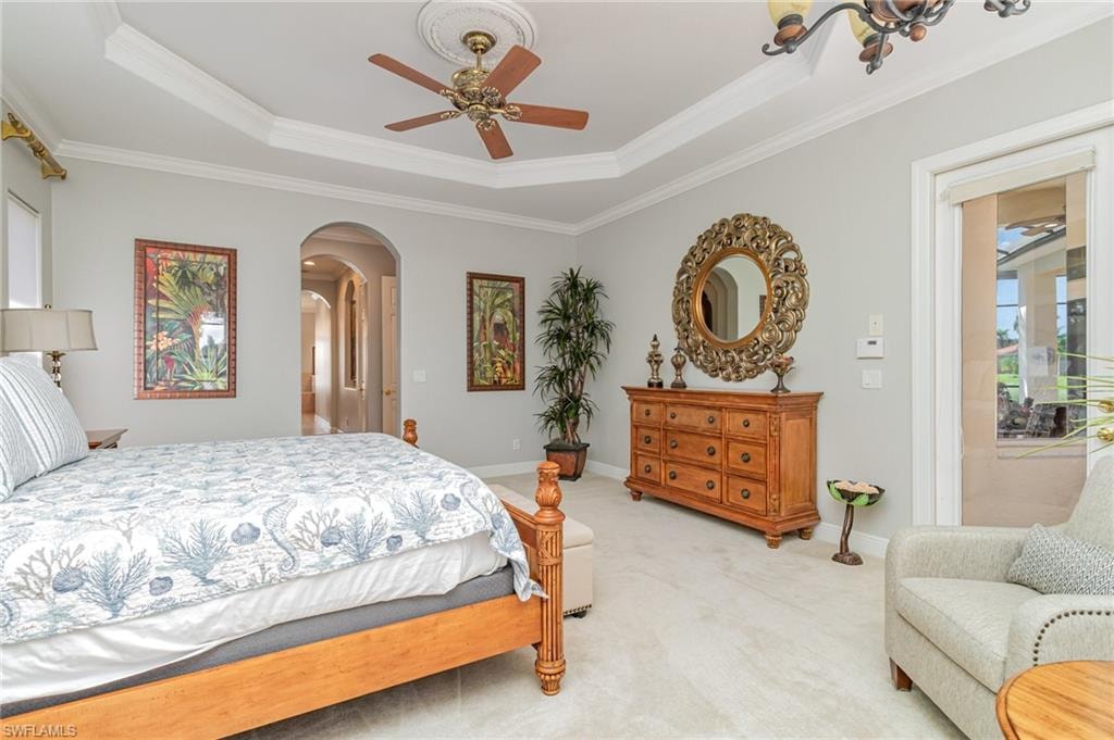 Carpeted bedroom featuring a tray ceiling, ornamental molding, ceiling fan, and arched walkways
