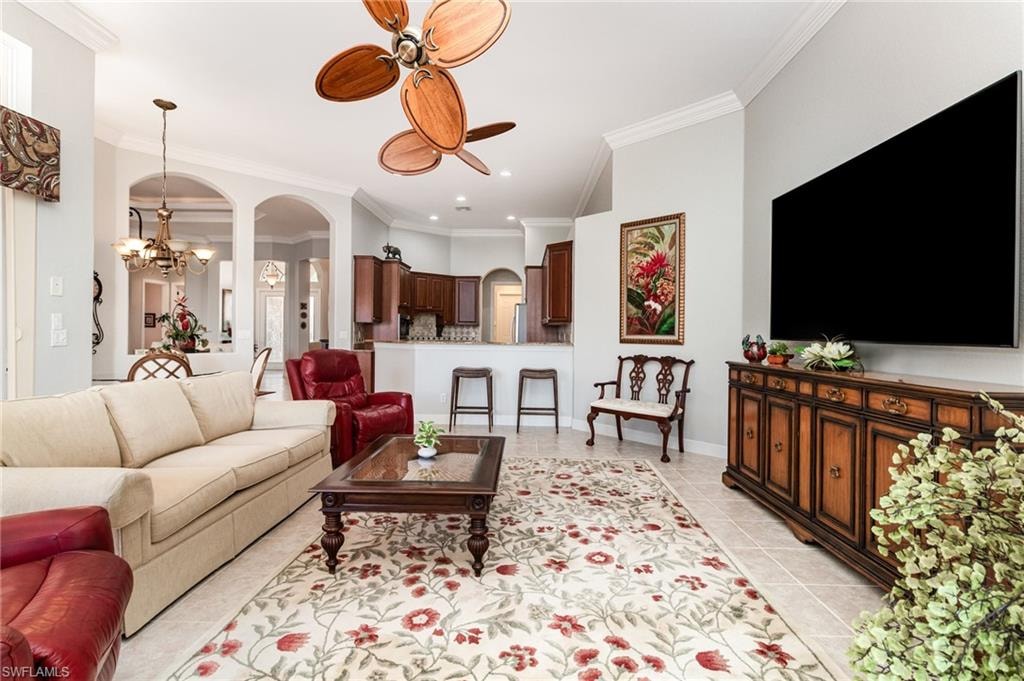 Living room with light tile patterned floors, arched walkways, a chandelier, ornamental molding, and ceiling fan
