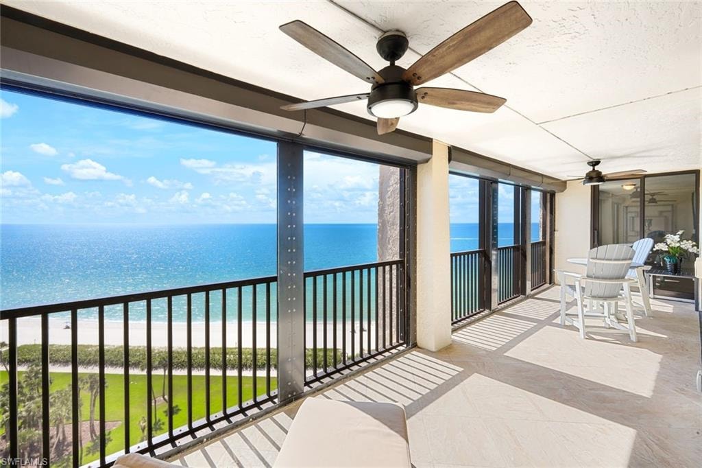 Balcony featuring view of water and beach and a ceiling fan