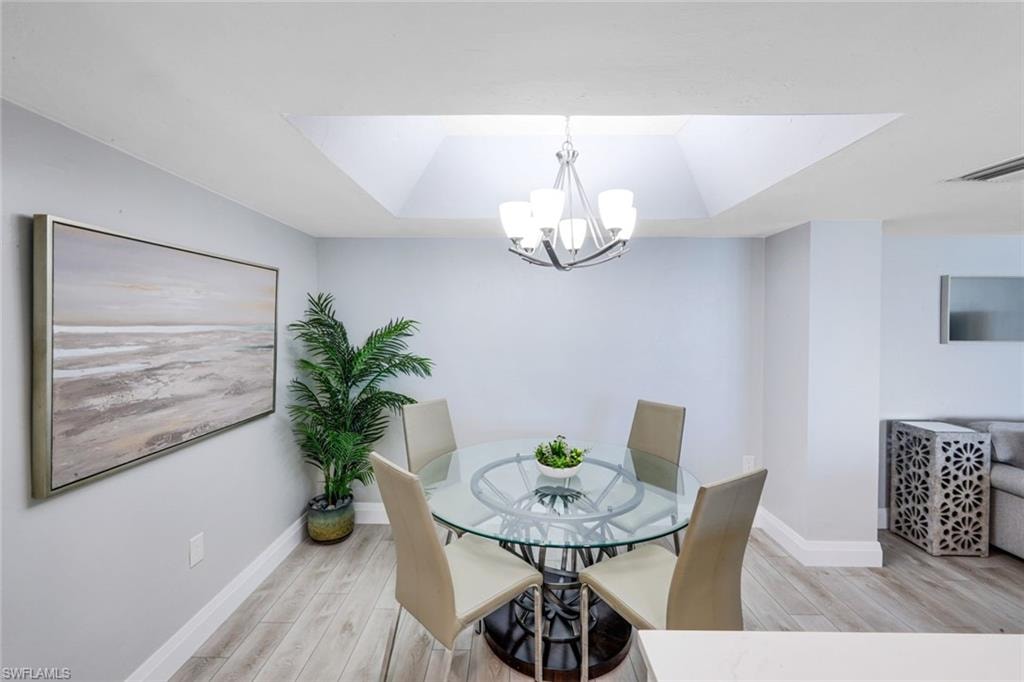 Dining area featuring a raised ceiling, light wood-type flooring, and a chandelier