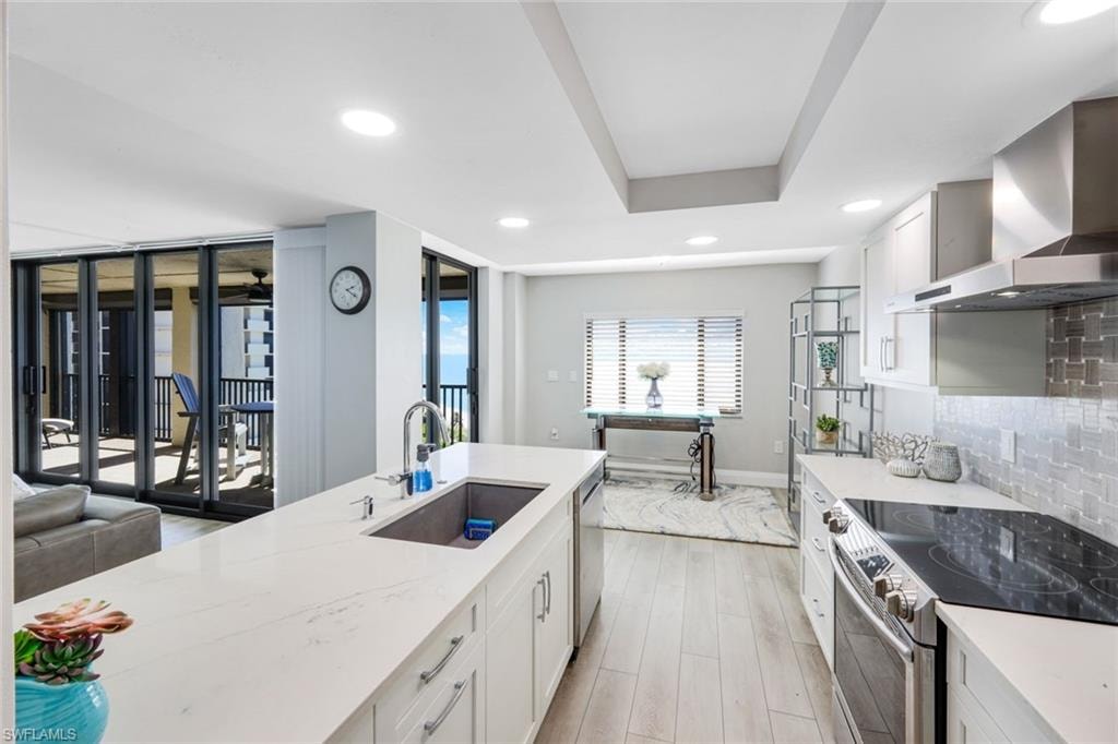 Kitchen featuring appliances with stainless steel finishes, white cabinetry, wall chimney exhaust hood, decorative backsplash, and recessed lighting
