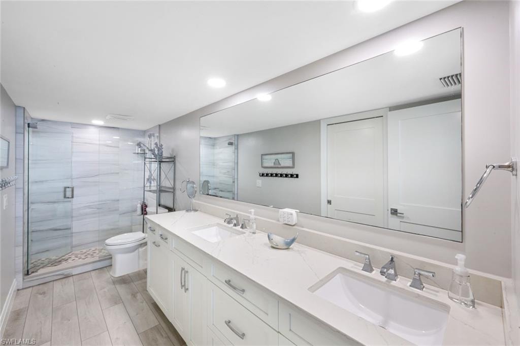 Bathroom featuring double vanity, a stall shower, light wood-type flooring, and recessed lighting