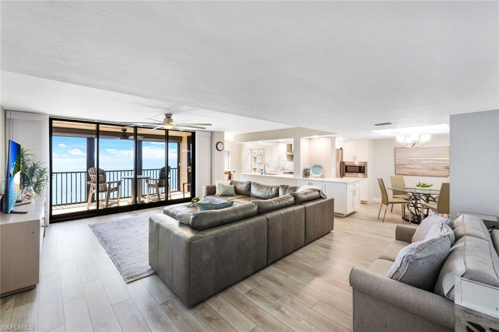 Living room featuring expansive windows, light wood-style flooring, ceiling fan, and a chandelier