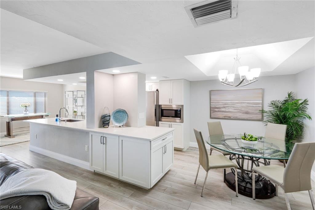 Kitchen featuring white cabinetry, a center island with sink, light wood finished floors, appliances with stainless steel finishes, and a chandelier