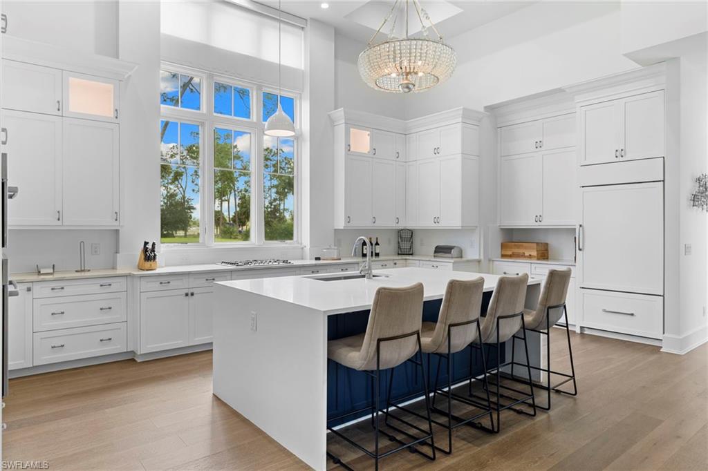 Kitchen with a high ceiling, white cabinets, an island with sink, light stone counters, and glass insert cabinets