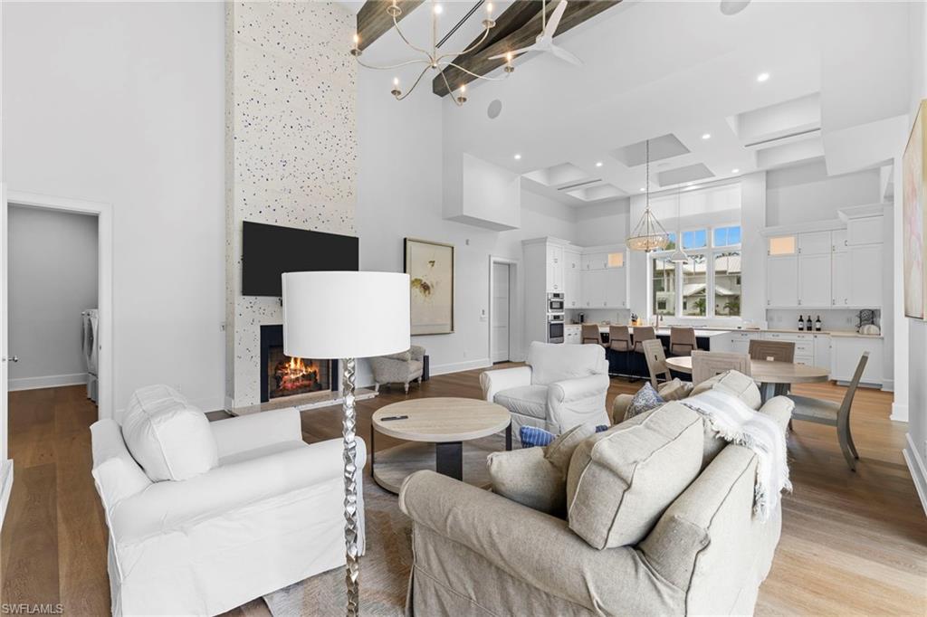 Living area featuring a chandelier, wood finished floors, a warm lit fireplace, and a towering ceiling