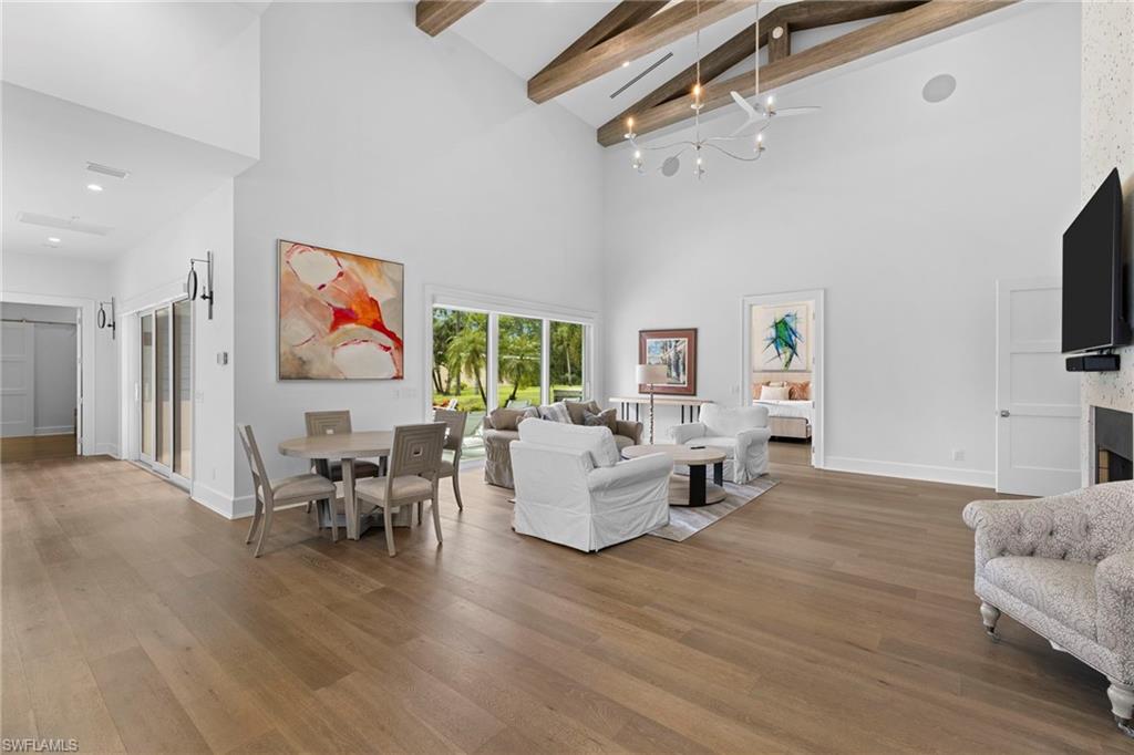 Living area featuring high vaulted ceiling, a fireplace, a chandelier, light wood-style flooring, and beamed ceiling