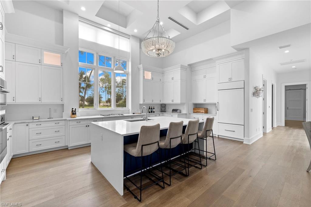 Kitchen with a kitchen island with sink, a chandelier, white cabinets, a kitchen breakfast bar, and a towering ceiling