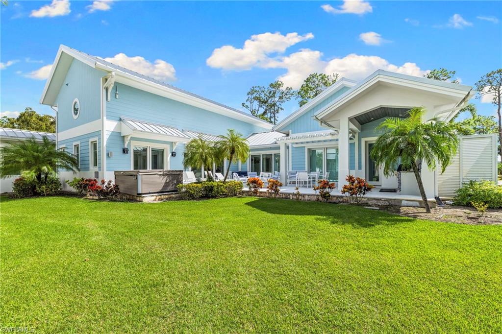 Rear view of property with a hot tub, a lawn, and a patio